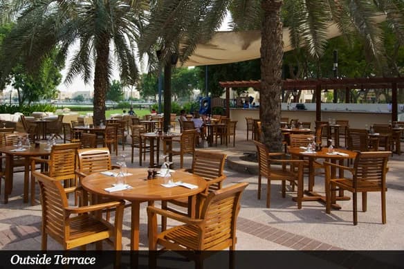 Wooden dining tables beneath palm trees on the outdoor terrace at Reform Social & Grill, The Lakes, Dubai